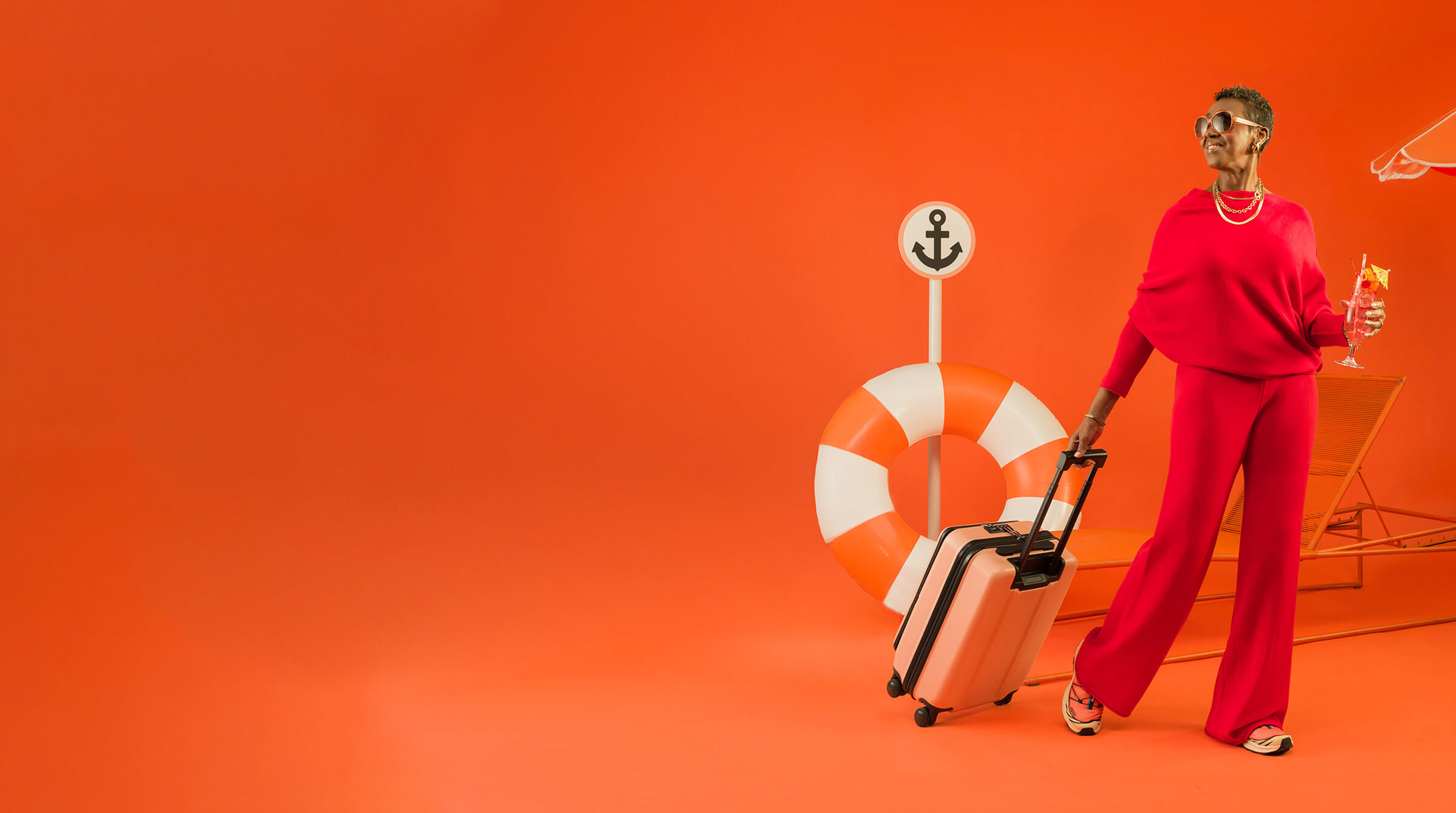 Person in red outfit with sunglasses holds a suitcase and a drink, standing before an orange background with a lifesaver, anchor sign, and lounger.