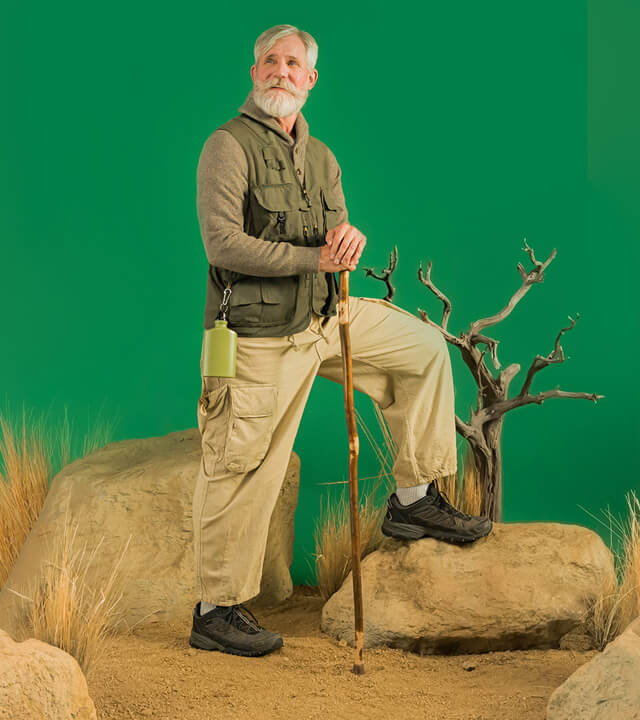 A man stands confidently on a rock against a vibrant green background, showcasing a serene outdoor setting.
