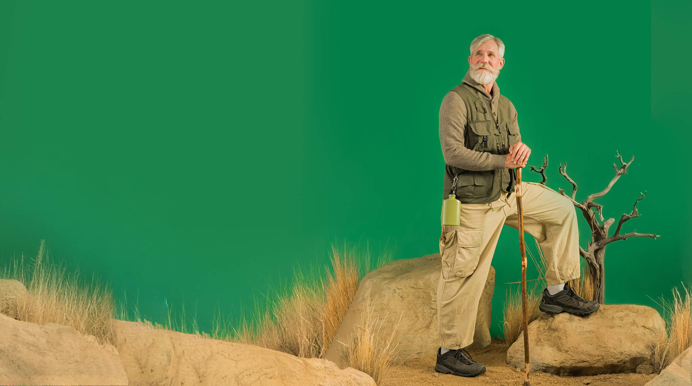 A man stands confidently on a rock against a vibrant green background, showcasing a serene outdoor setting.