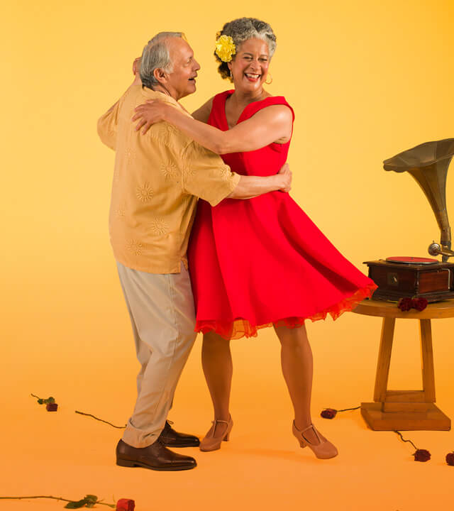 An elderly couple joyfully dancing together against a vibrant yellow background, showcasing their love and happiness.