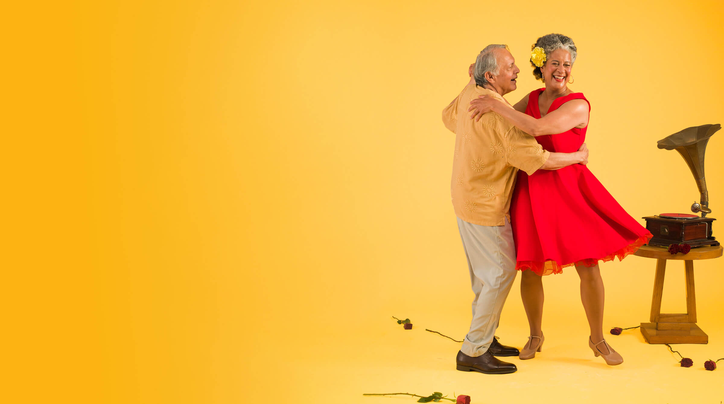 An elderly couple joyfully dancing together against a vibrant yellow background, showcasing their love and happiness.